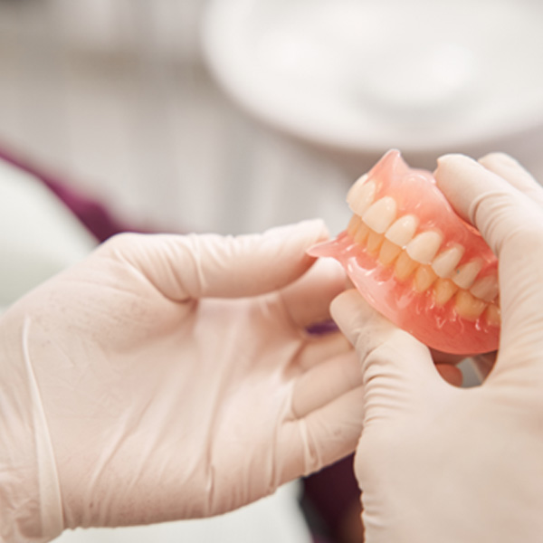 Gloved hands holding a pair of dentures