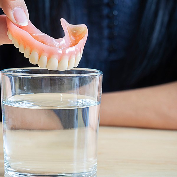 a person putting their denture in a glass of water