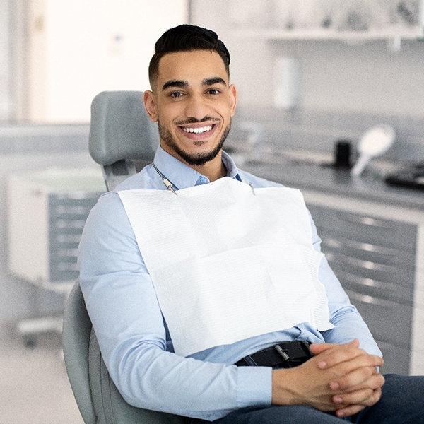 Man in dental chair smiling with hands folded 