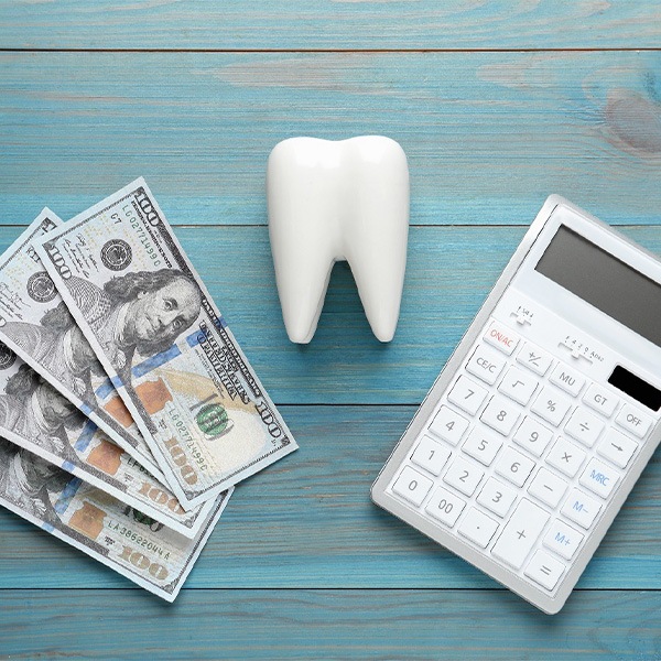 Several hundred dollar bills, a model tooth, and a calculator arranged on a blue wooden table