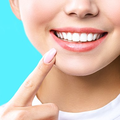 Nose-to-neck view of a woman with pink nails touching her pointer finger to her smile with electric light blue background