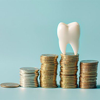 A large model tooth sitting on top of a few piles of coins with a light aquamarine background